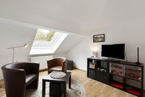 Ein modernes Wohnzimmer mit Oberlicht, Fernseher, Sofa und einem kleinen Tisch.