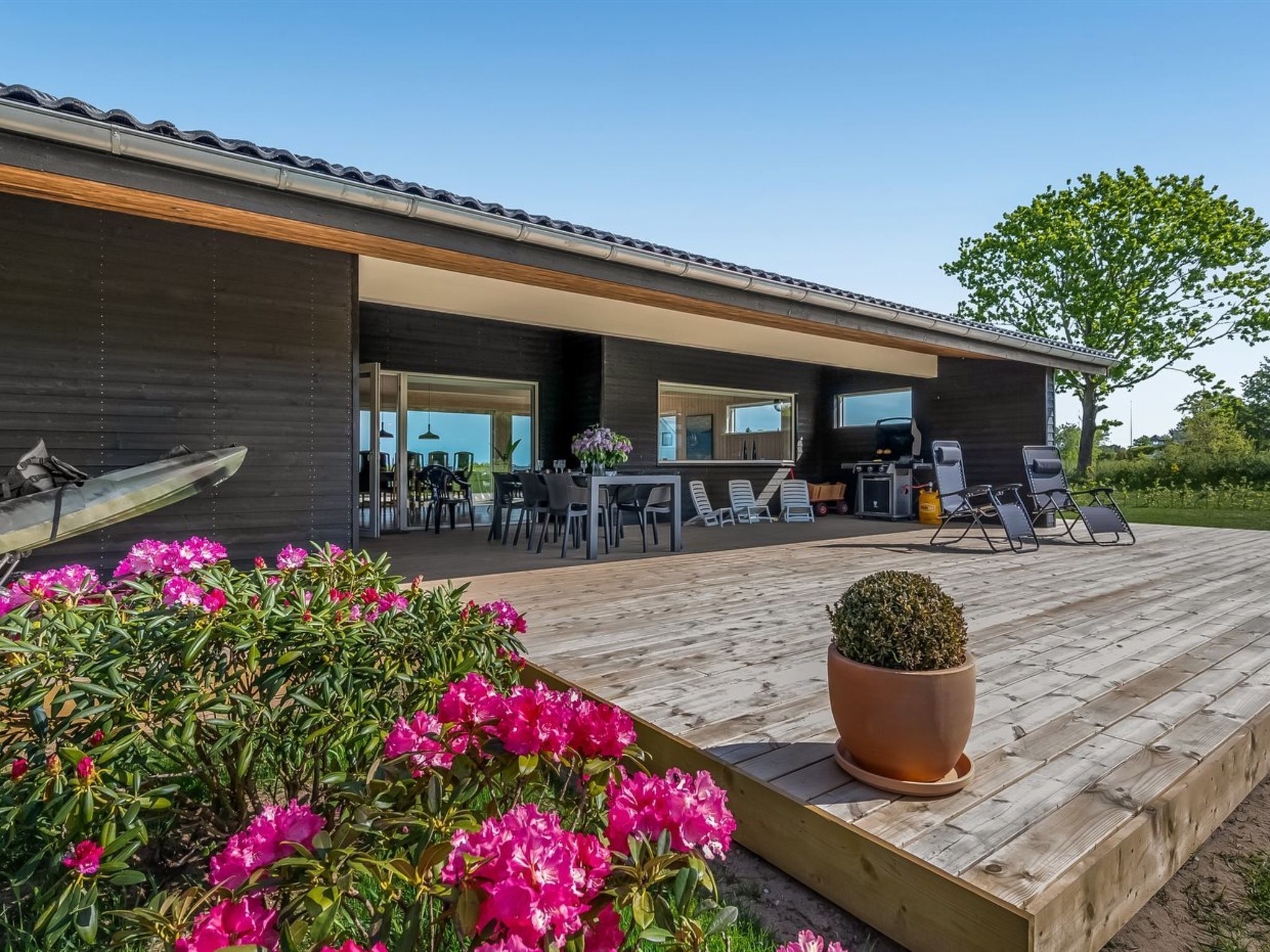 A modern house with a wooden deck, outdoor seating, and a kayak.