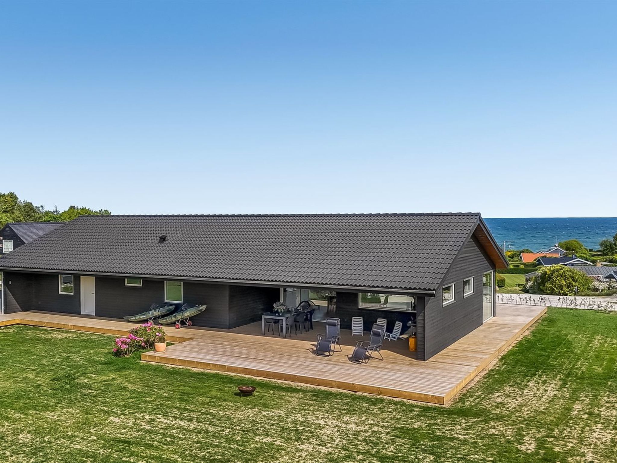 Ein modernes, zweistöckiges Haus mit flachem Dach, einer Terrasse mit Gartenmöbeln und Blick auf das Meer.