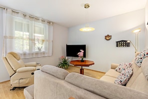 A living room with a sofa, a recliner, a TV, a small table with a plant, and a floor lamp. - Apartment '2 Zimmer 69 Qm' with Shared Terrace, Shared Garden and Wi-Fi (Mittenwalde)