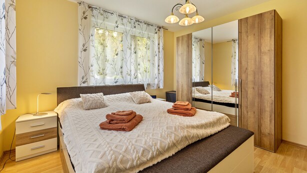 Een slaapkamer met een bed, nachtkastje, lamp en een grote spiegel.