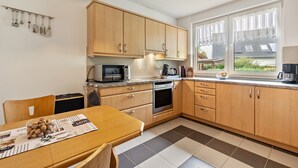 Een moderne keuken met houten kasten, een eettafel en een raam met gordijnen.