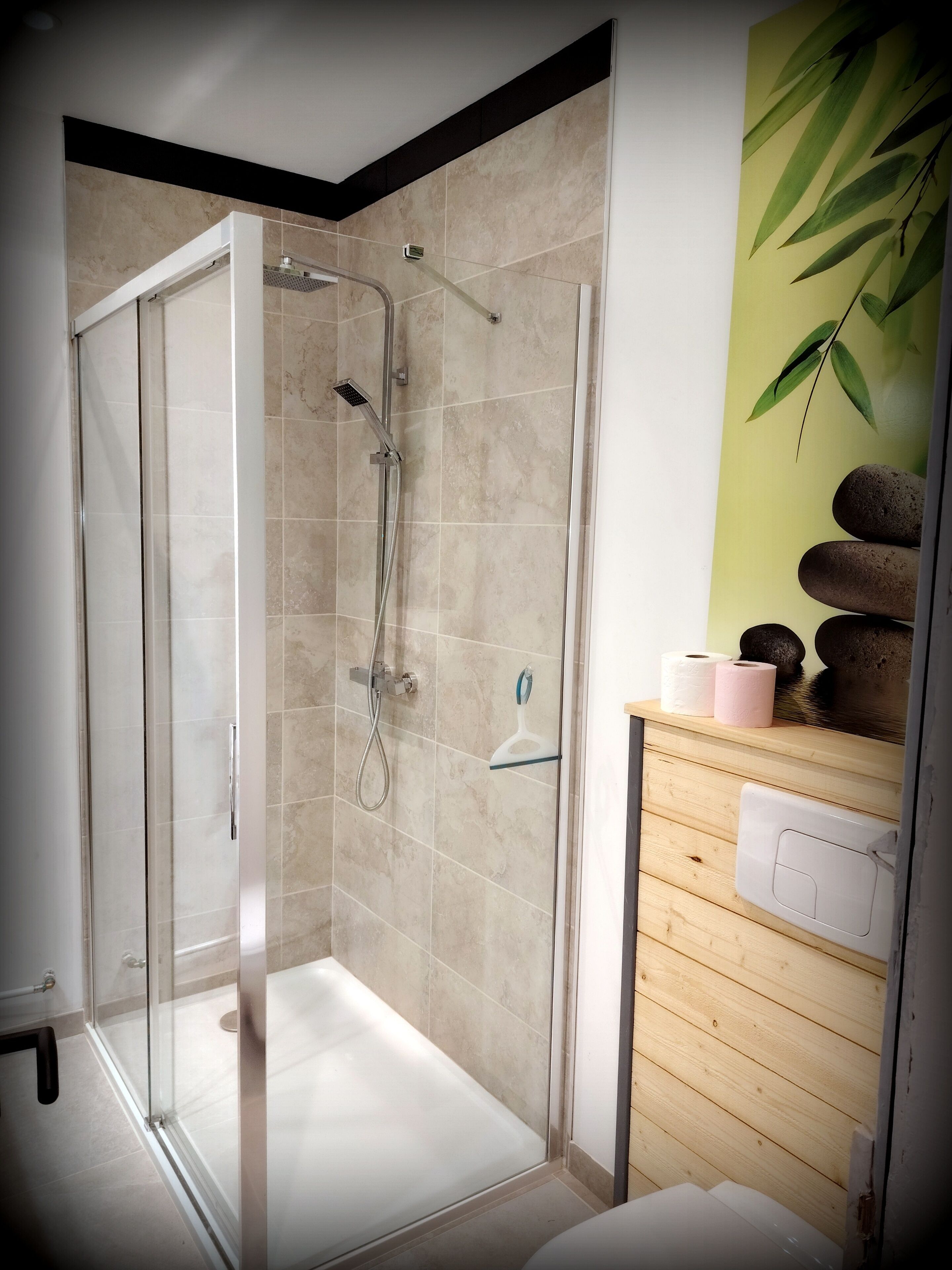 A glass-enclosed shower with a handheld showerhead and a wall-mounted faucet.