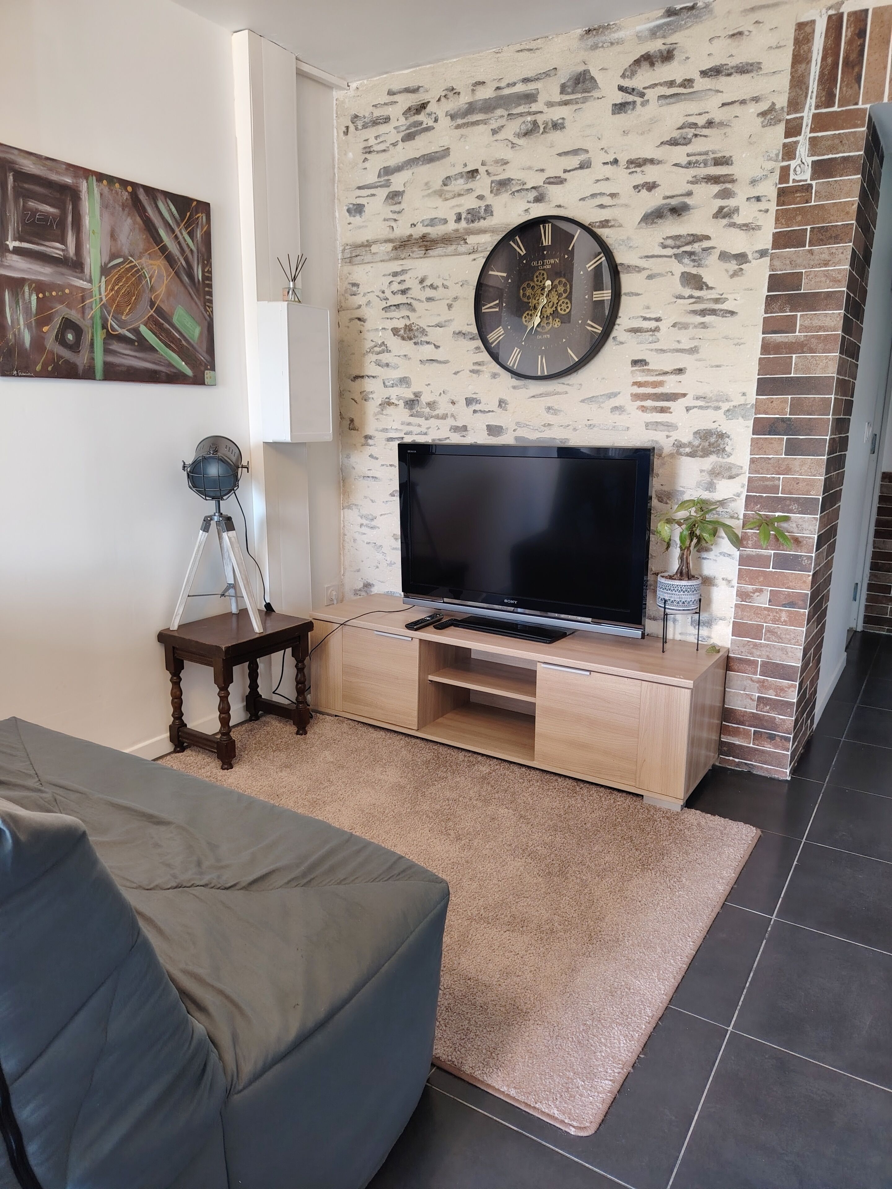 A living room with a flat-screen TV on a wooden TV stand, a clock on the wall, and a painting on the wall.