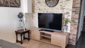 A living room with a flat-screen TV on a wooden TV stand, a clock on the wall, and a painting on the wall.
