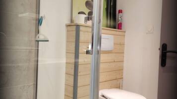 A modern bathroom with a glass shower enclosure, a toilet, and a wooden cabinet with toiletries.