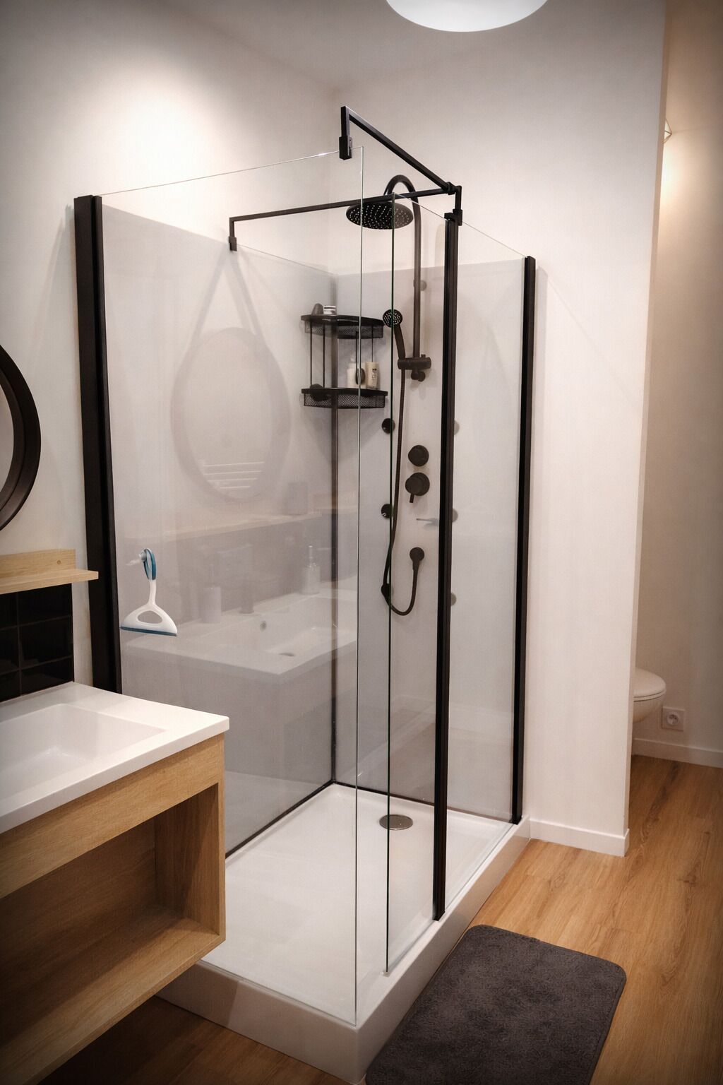 Un baño moderno con ducha envuelta en vidrio, tocador de madera y lavamanos blanco.