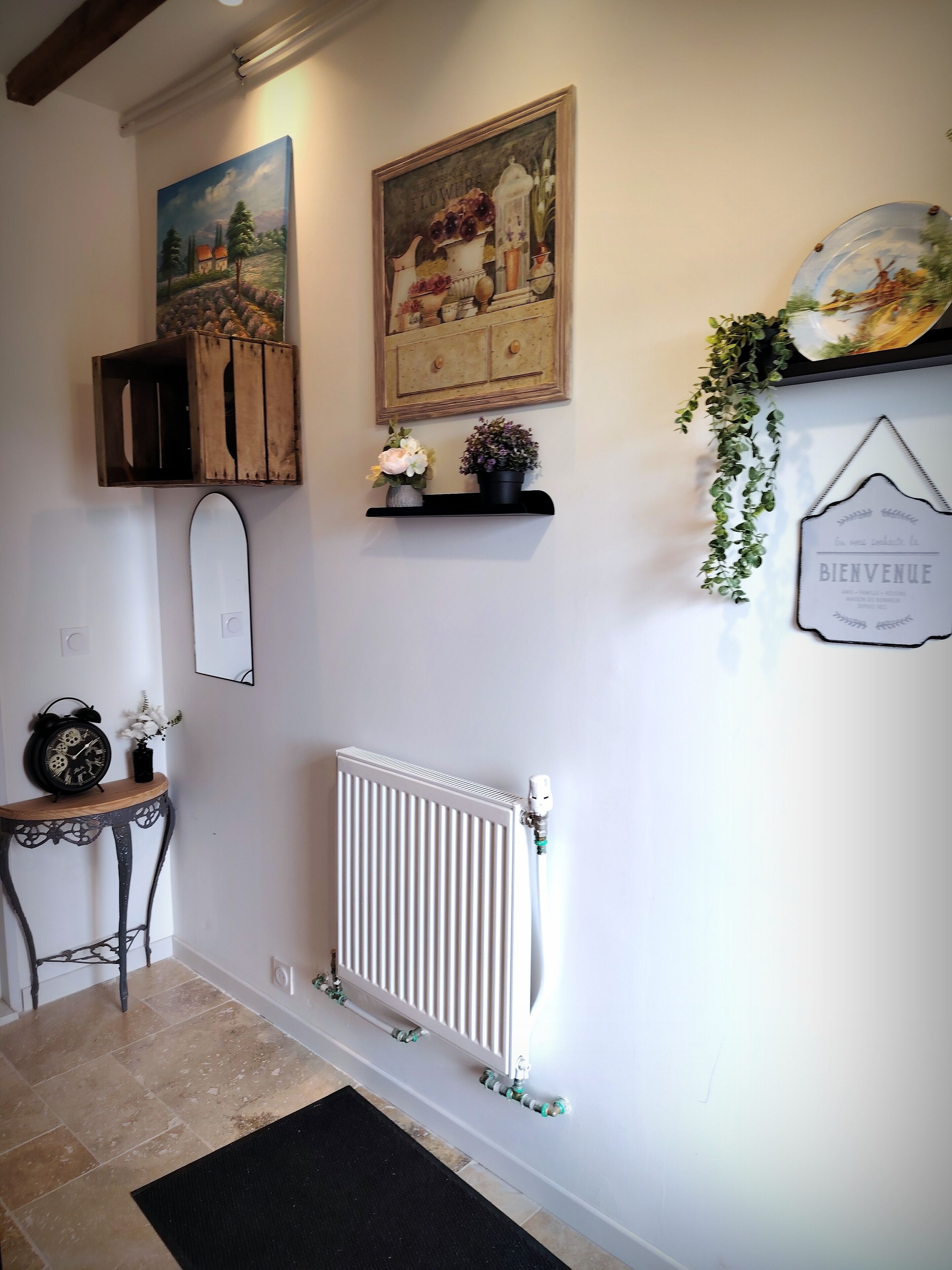 A hallway with a rustic wooden shelf holding a vintage clock and a framed painting of a rural scene.