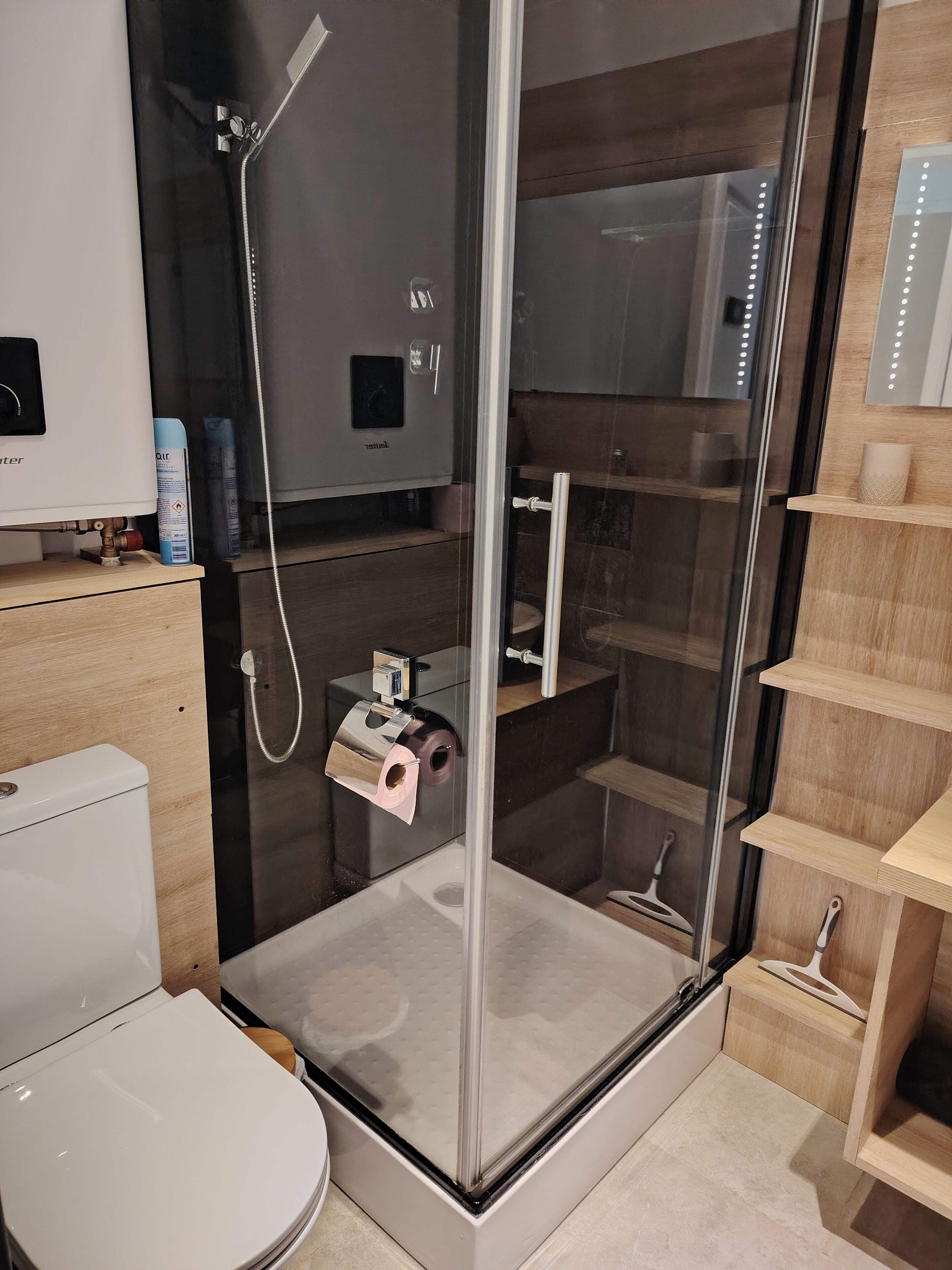 Une salle de bain moderne dotée d’une douche à parois de verre, de toilettes et d’un meuble-lavabo avec des étagères.