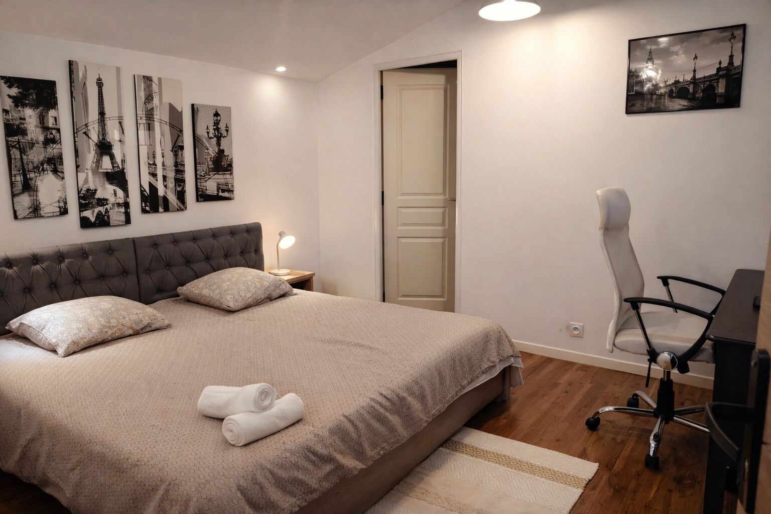 A bedroom with a large bed, a desk with a chair, and artwork on the walls.