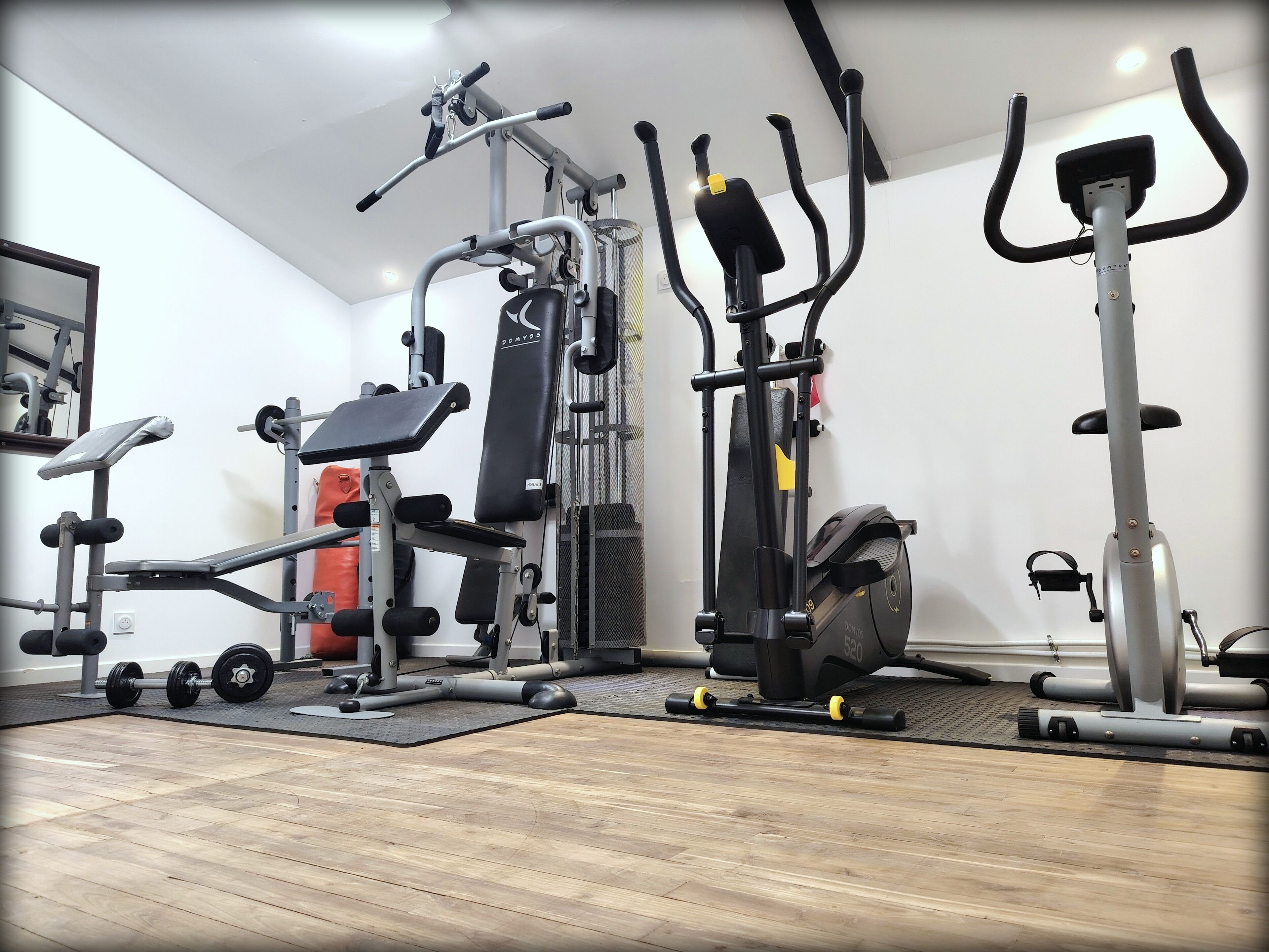 Een huisgym met een bankdrukapparaat, een hometrainer en een loopband.