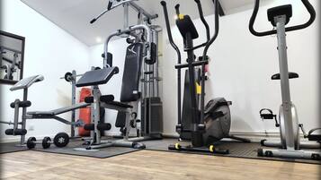 Een huisgym met een bankdrukapparaat, een hometrainer en een loopband.
