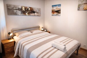 Uma cama bem arrumada com roupa de cama listrada, duas luminárias de cabeceira e uma mesa de cabeceira com gaveta.