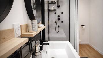 Een moderne badkamer met een witte wasbak, een spiegel, een handdoekrek, een douche met glazen deur en een toilet.