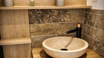 Un baño moderno con un lavabo redondo color beige, estantes de madera y una toalla negra.