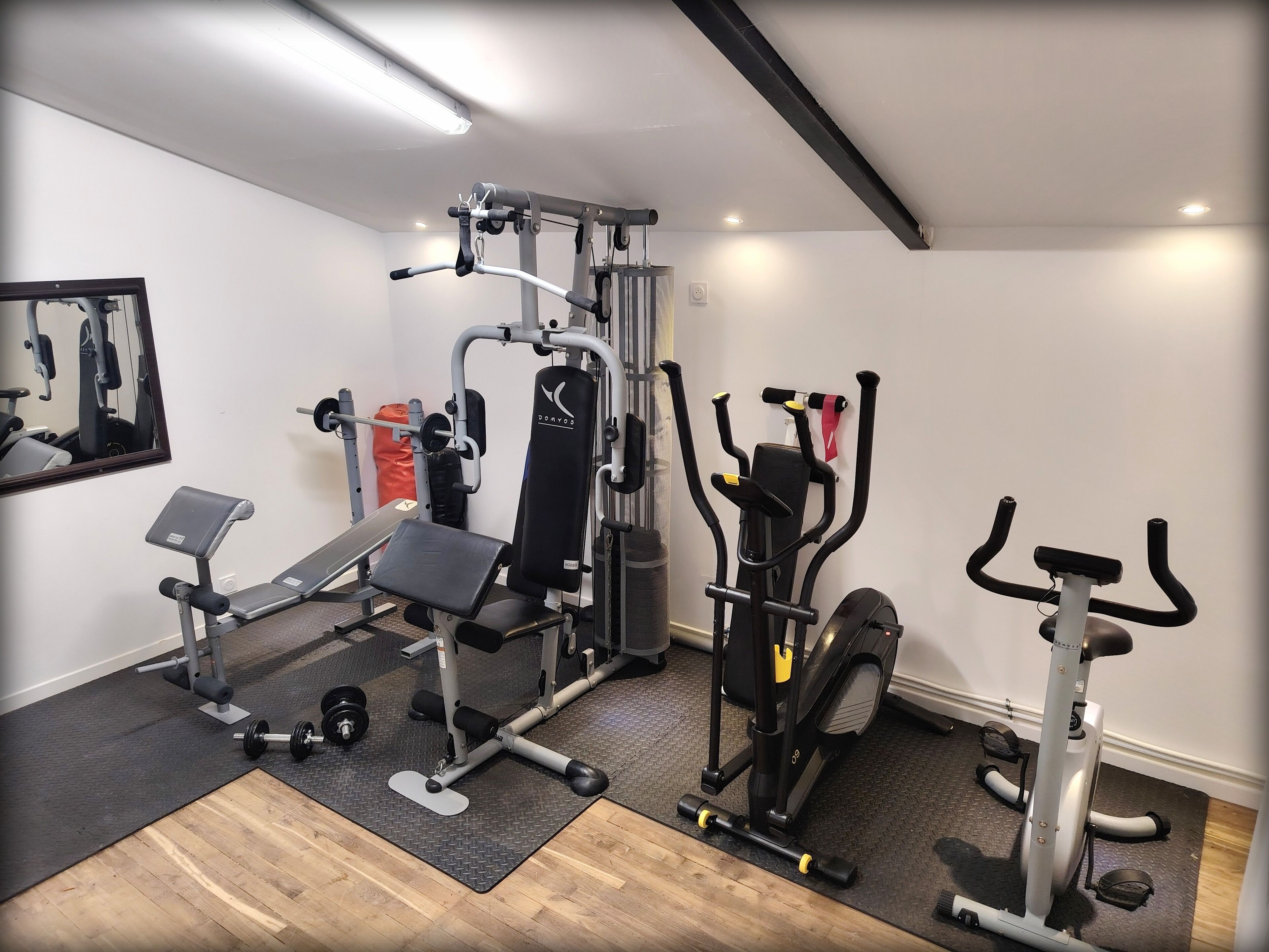 Un gimnasio en casa con una prensa de banca, una jaula para sentadillas, una máquina de poleas y una bicicleta estática.