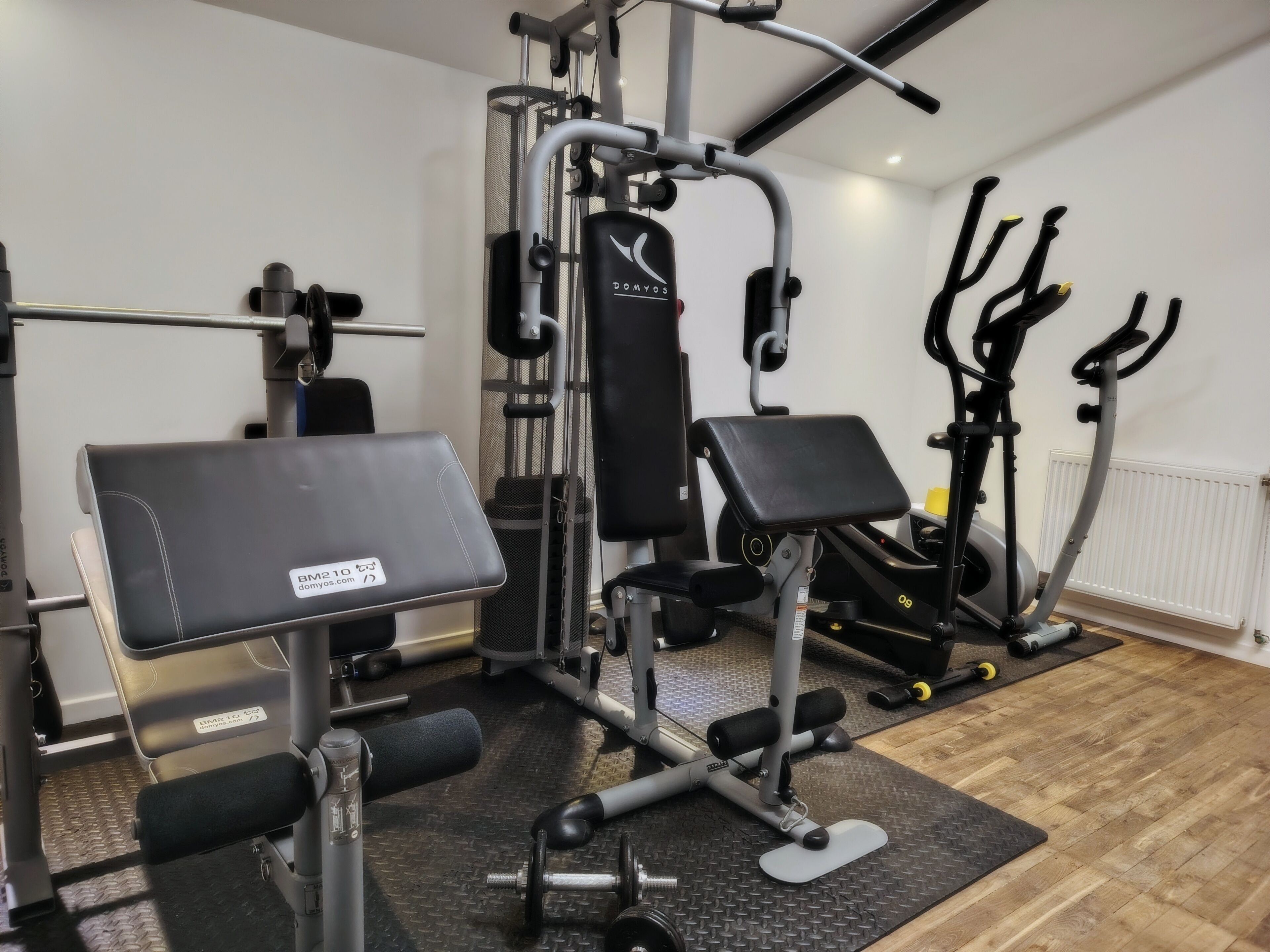 Une salle de sport équipée d’un banc de développé couché, d’une machine à câbles et d’un appareil elliptique.