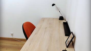 Una habitación minimalista con una mesa de madera, una sola silla, una lámpara de escritorio, un reloj y un cuadro en la pared.
