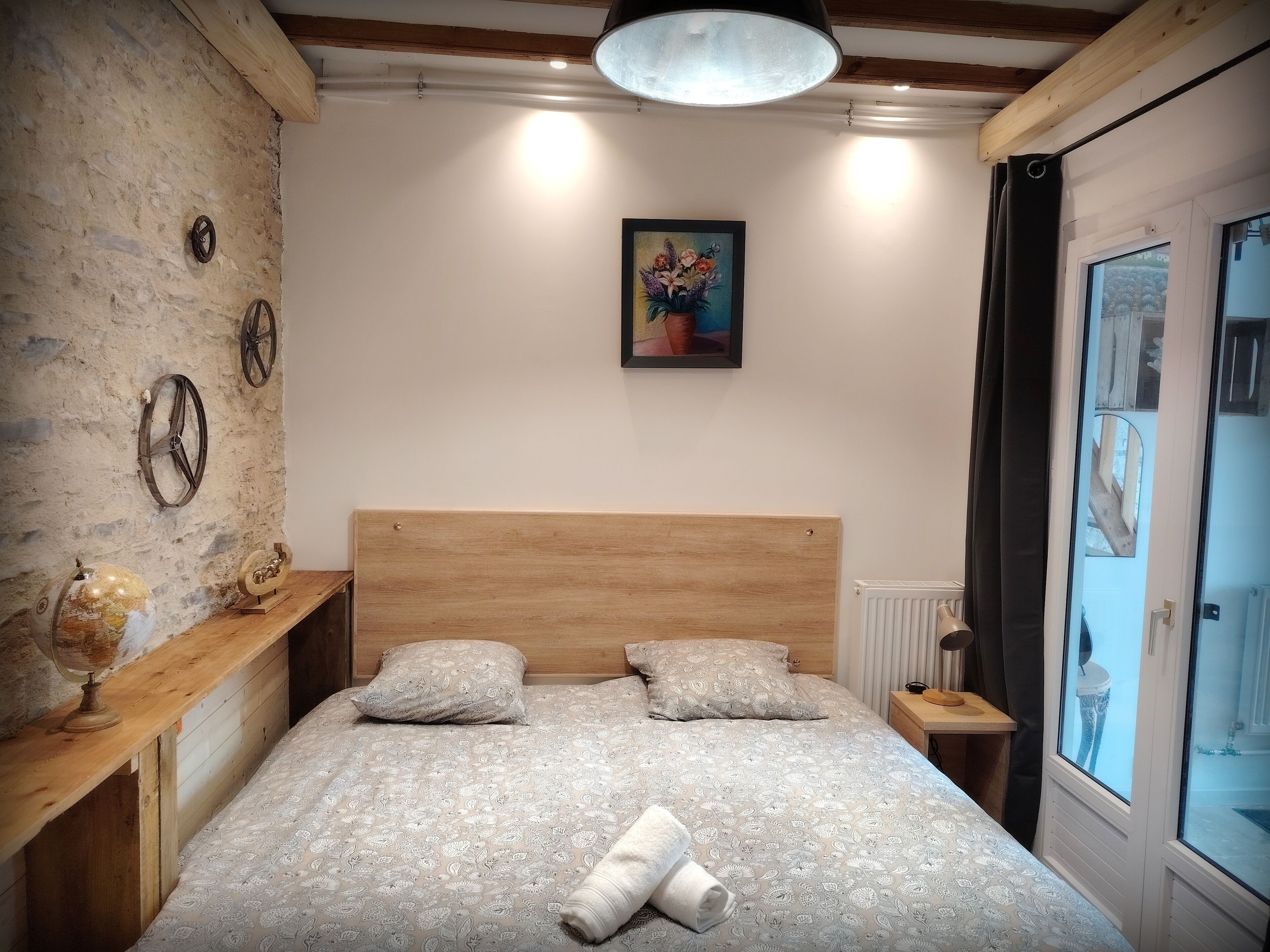 A bedroom with a wooden headboard, a bed with patterned bedding, a globe, and a painting on the wall.