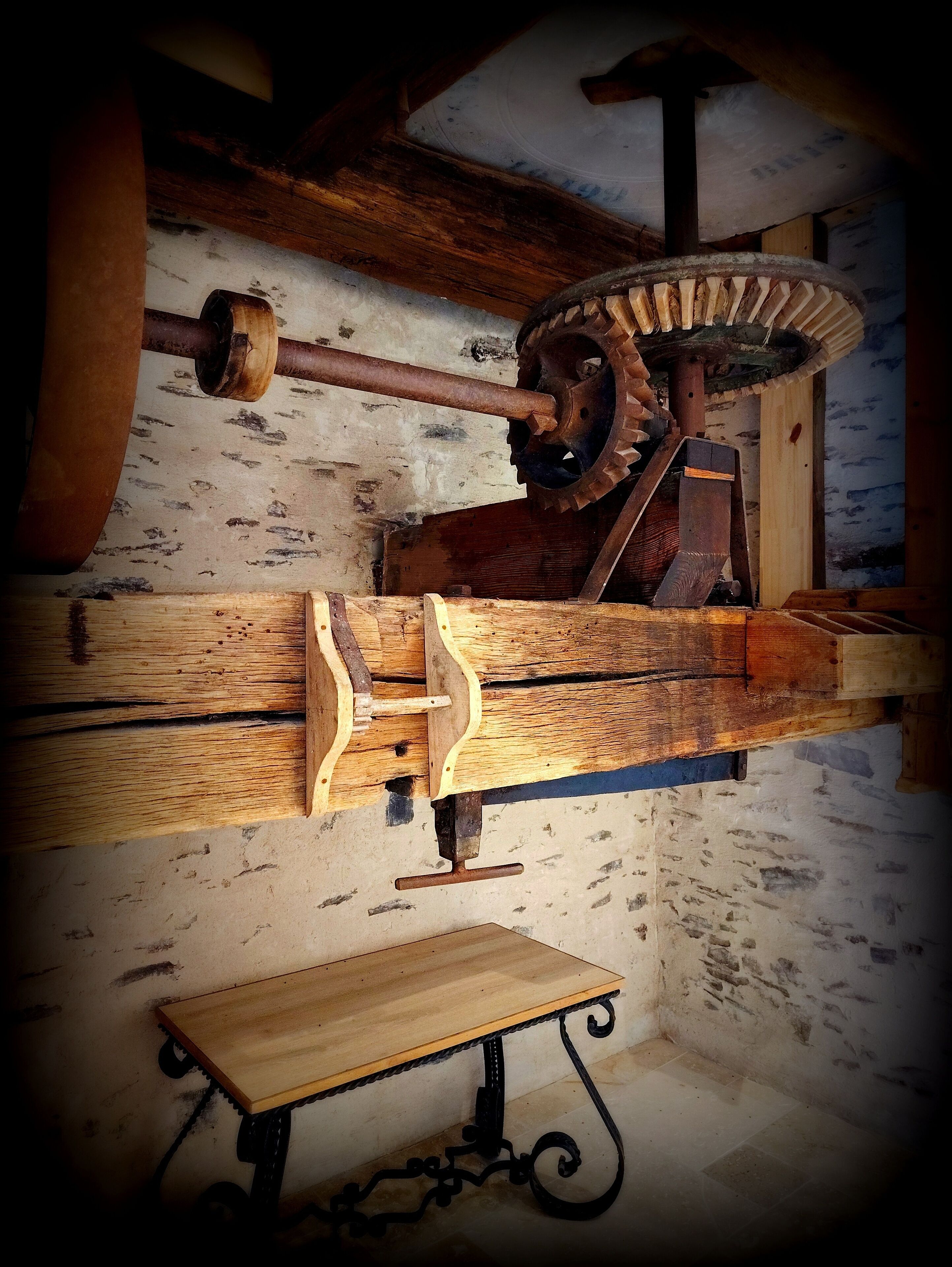 A vintage mechanical device, possibly a lathe, in a workshop with a wooden workbench and a metal frame.