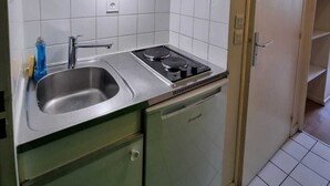 A compact kitchen with a sink, stove, and green cabinets. - Résidence hôtelière ERASMUS (Malakoff)