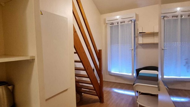 A compact living space with a wooden staircase, a kitchenette, and a small seating area. - Résidence hôtelière ERASMUS (Malakoff)