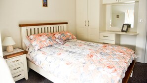 A bedroom with a bed, a nightstand, a dresser, and a mirror. - Skellig Fuchsia Lodge Ballinskelligs (Ballinskelligs)