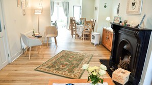A cozy living room with a fireplace, a dining area, and a hallway leading to an open space. - Skellig Fuchsia Lodge Ballinskelligs (Ballinskelligs)