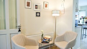 A room with two beige armchairs, a small round table with books and a vase, and a floor lamp. - Skellig Fuchsia Lodge Ballinskelligs (Ballinskelligs)