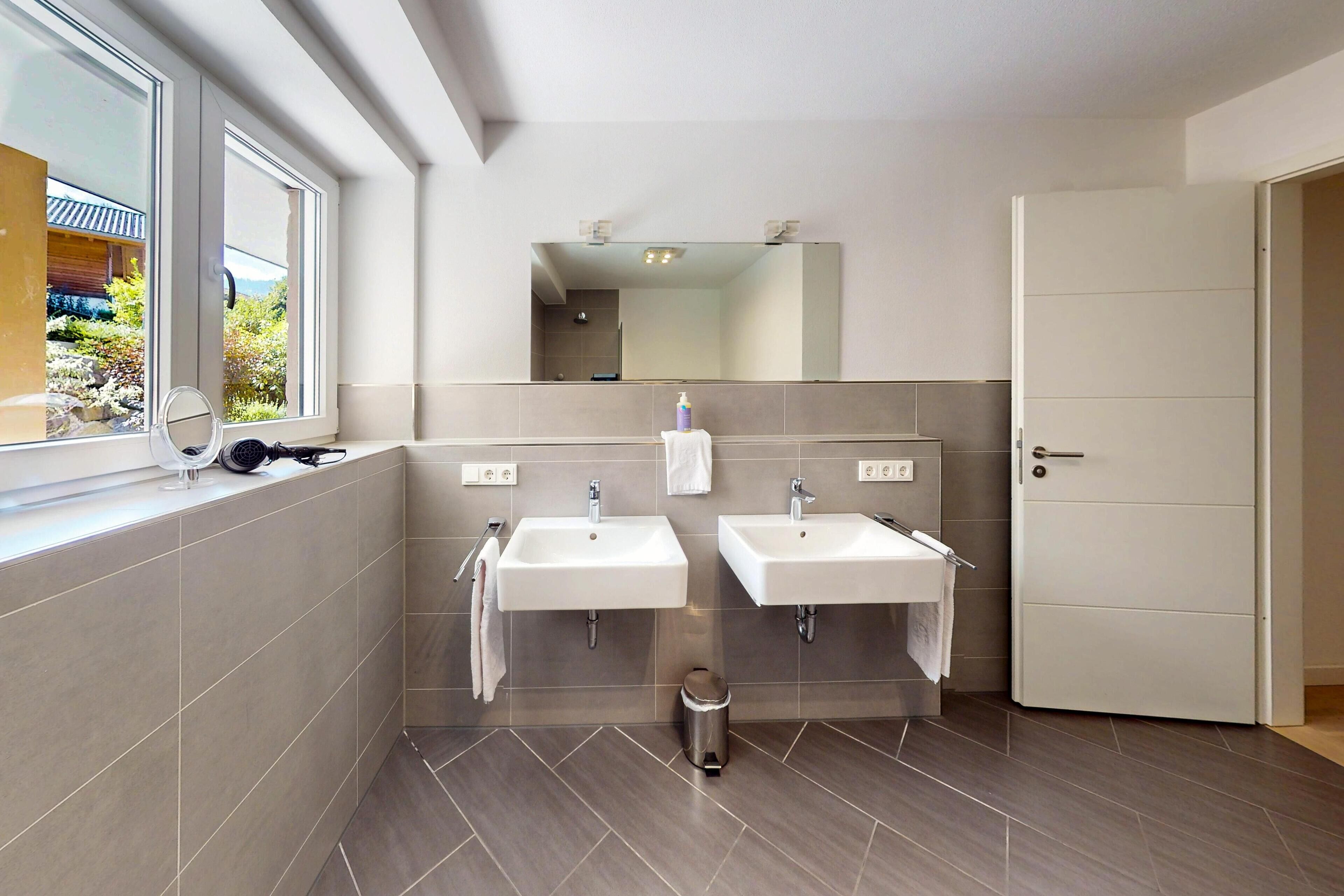 Een moderne badkamer met twee wasbakken, een spiegel en een raam.