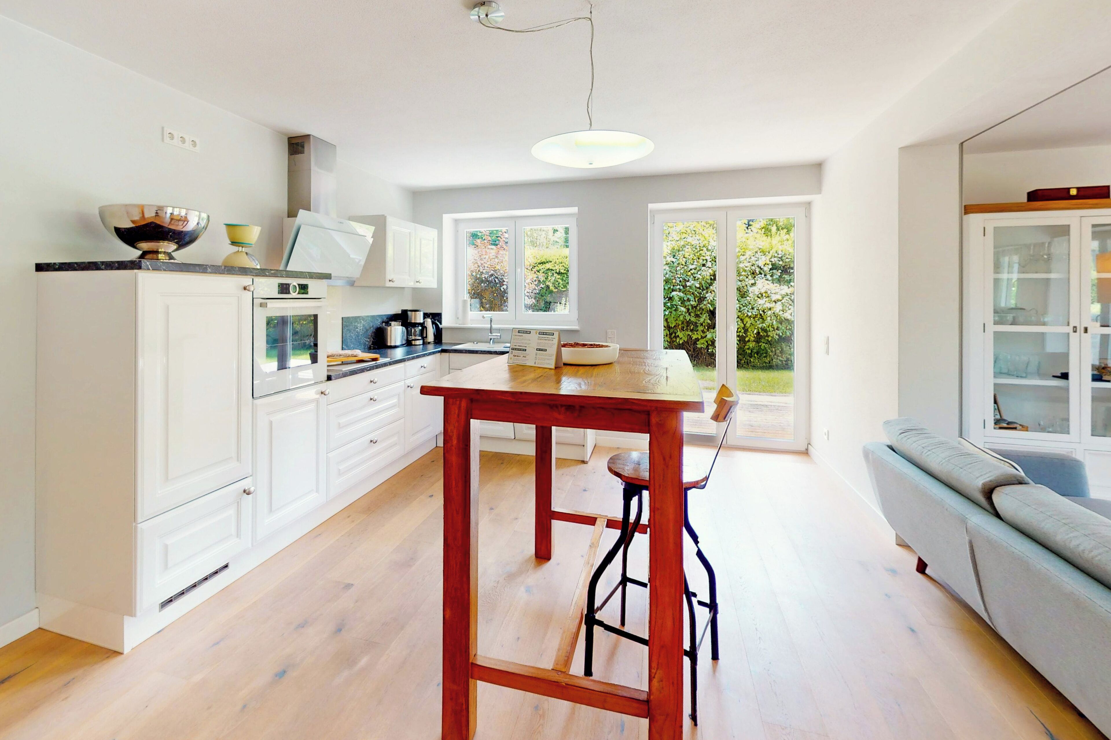 Een moderne keuken met witte kastjes, een houten tafel en een ingebouwde oven. Een groot raam zorgt voor natuurlijk licht en uitzicht op groen.
