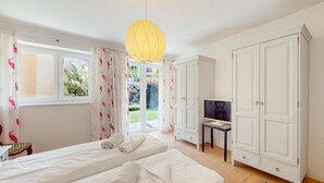 Un dormitorio con dos camas, televisión, armario y vistas a un jardín.
