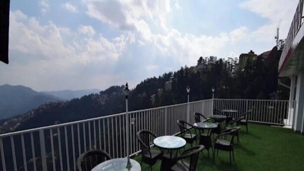 A balcony with artificial grass, wicker chairs, and tables, overlooking a mountainous landscape. - the town ville  (Shimla)