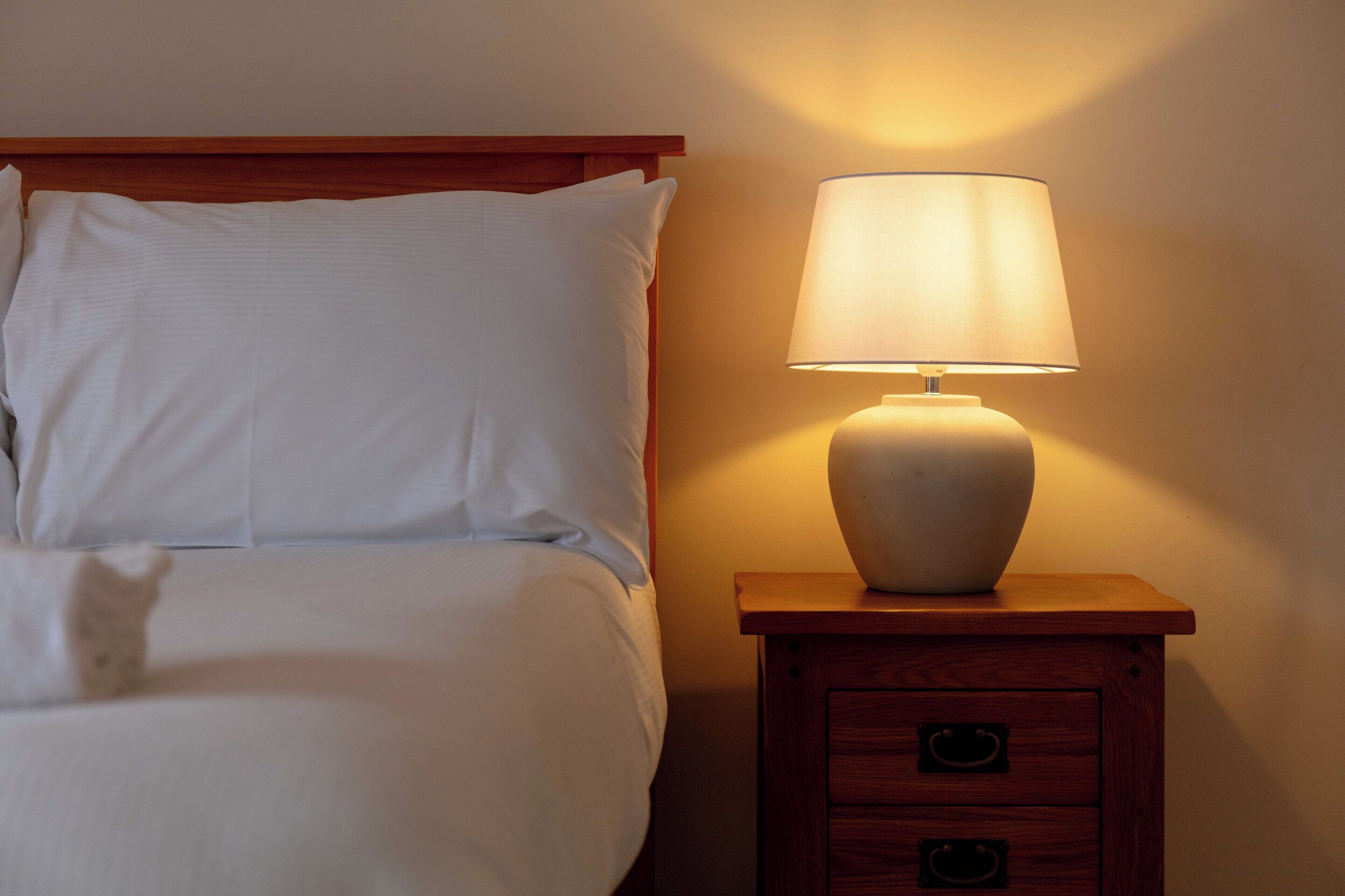 A neatly made bed with white linens and a bedside table with a lamp.