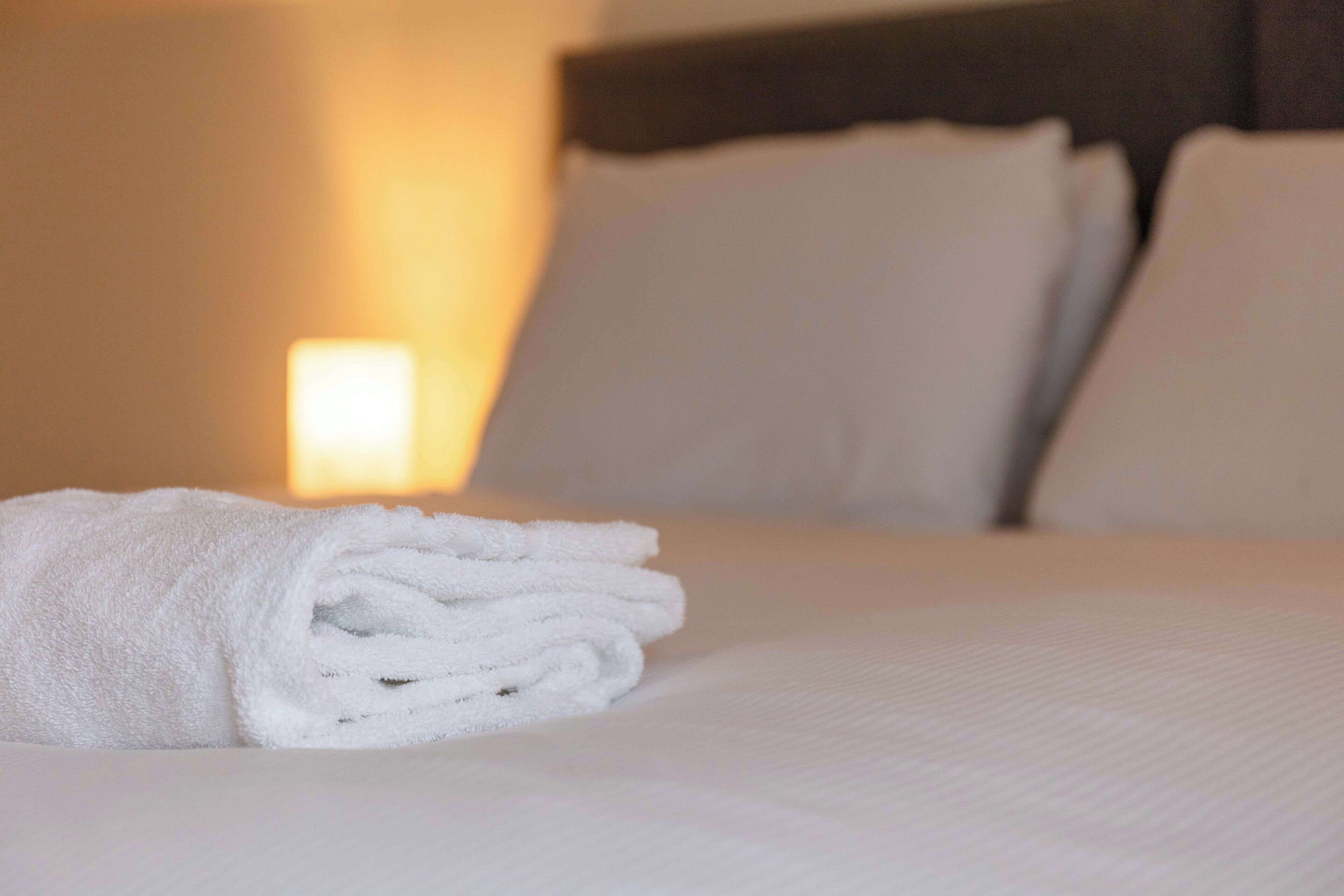 Una cama bien tendida con sábanas y almohadas blancas, una lámpara de noche y un cabecero oscuro.