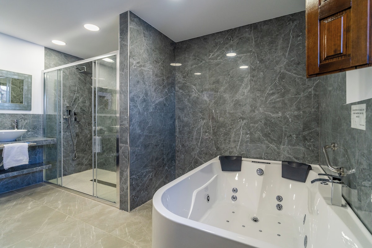 A modern bathroom with a glass-enclosed shower, a white bathtub with multiple jets, and a marble-tiled wall.