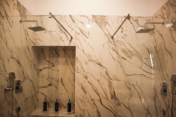 Un baño moderno con paredes de mármol, ducha con mampara de vidrio y estante con artículos de tocador.