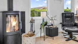 Un salon chaleureux avec un poêle à bois, un fauteuil en cuir confortable et une vue sur le jardin grâce à de grandes fenêtres.