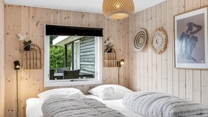 Une chambre avec un grand lit, une fenêtre donnant sur un paysage verdoyant, un luminaire suspendu et des éléments de décoration fixés au mur.