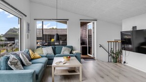 Een moderne woonkamer met een modulaire bank, een salontafel en een aan de muur bevestigde televisie.