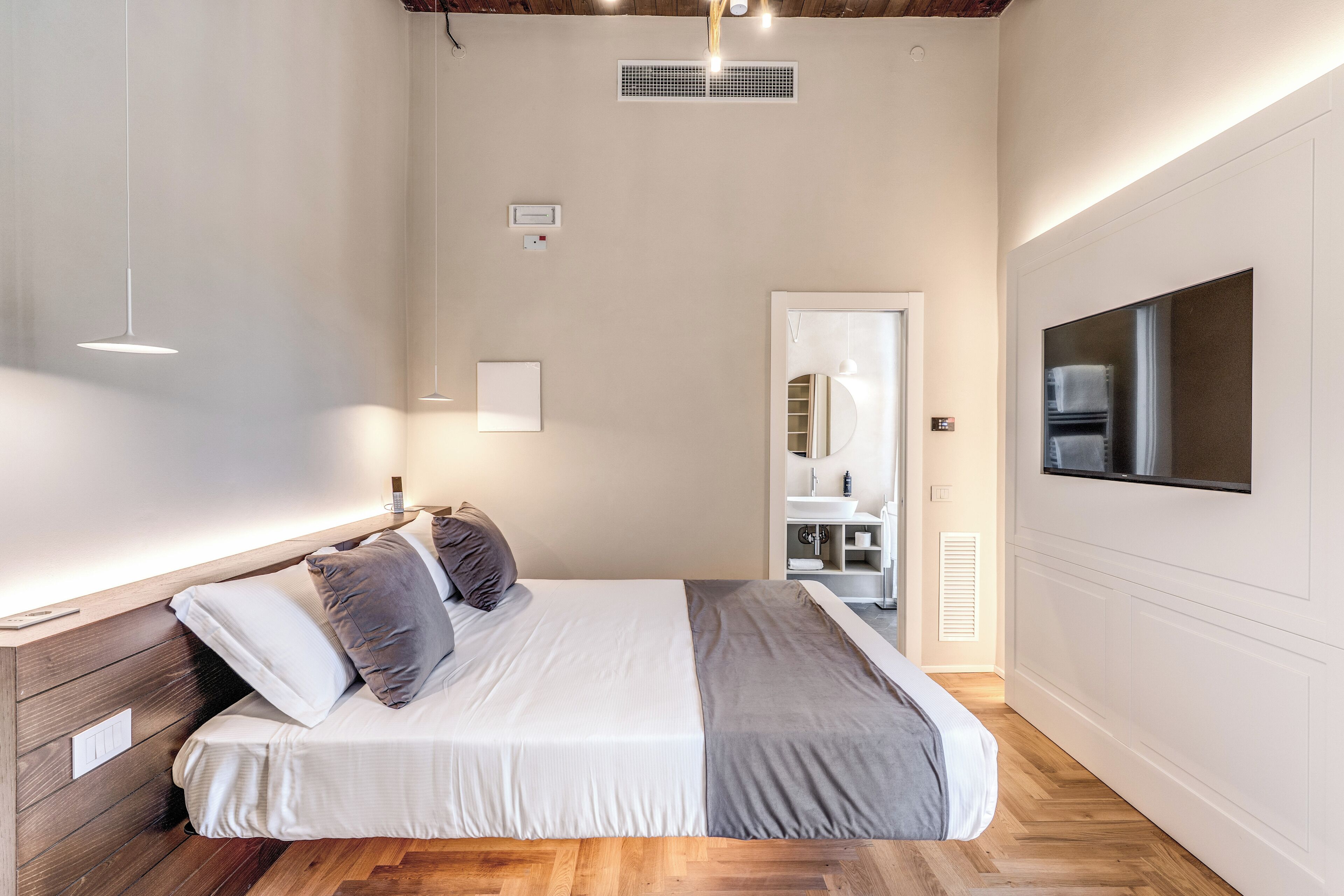 Una camera da letto con un letto, comodini, un armadio, uno specchio e una TV a parete.