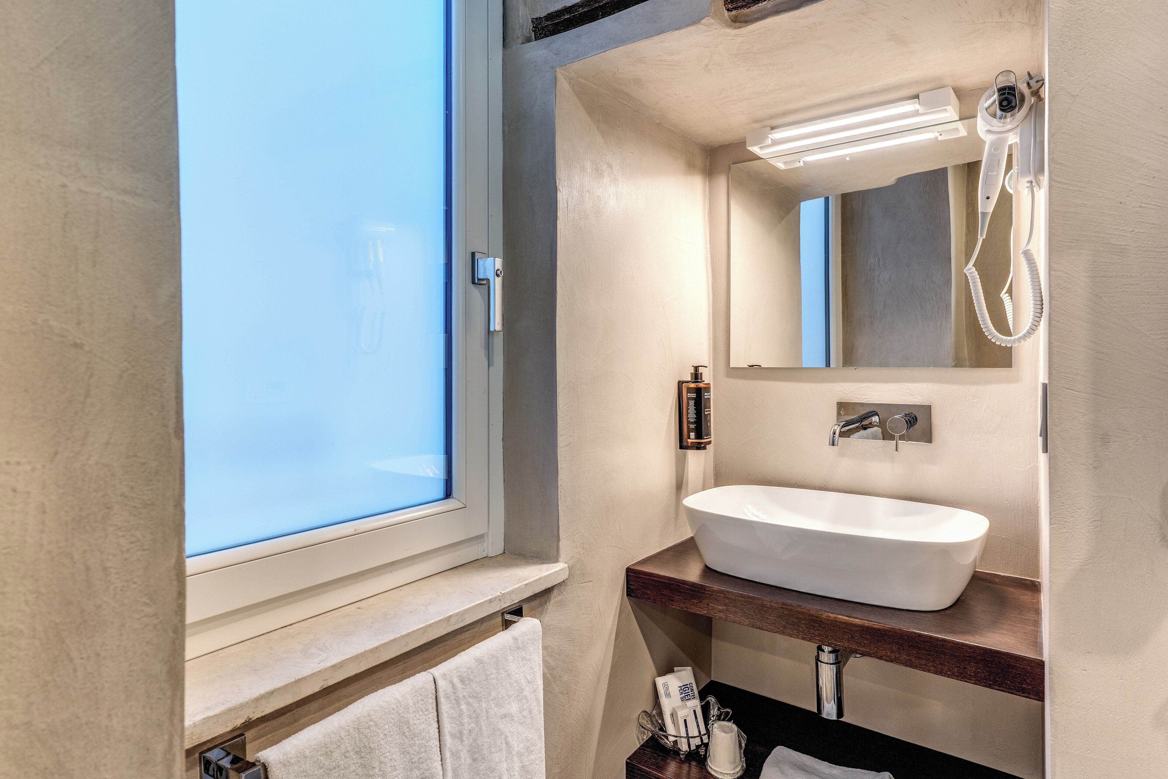 A bathroom with a large window, a white sink, a mirror, and a hairdryer.