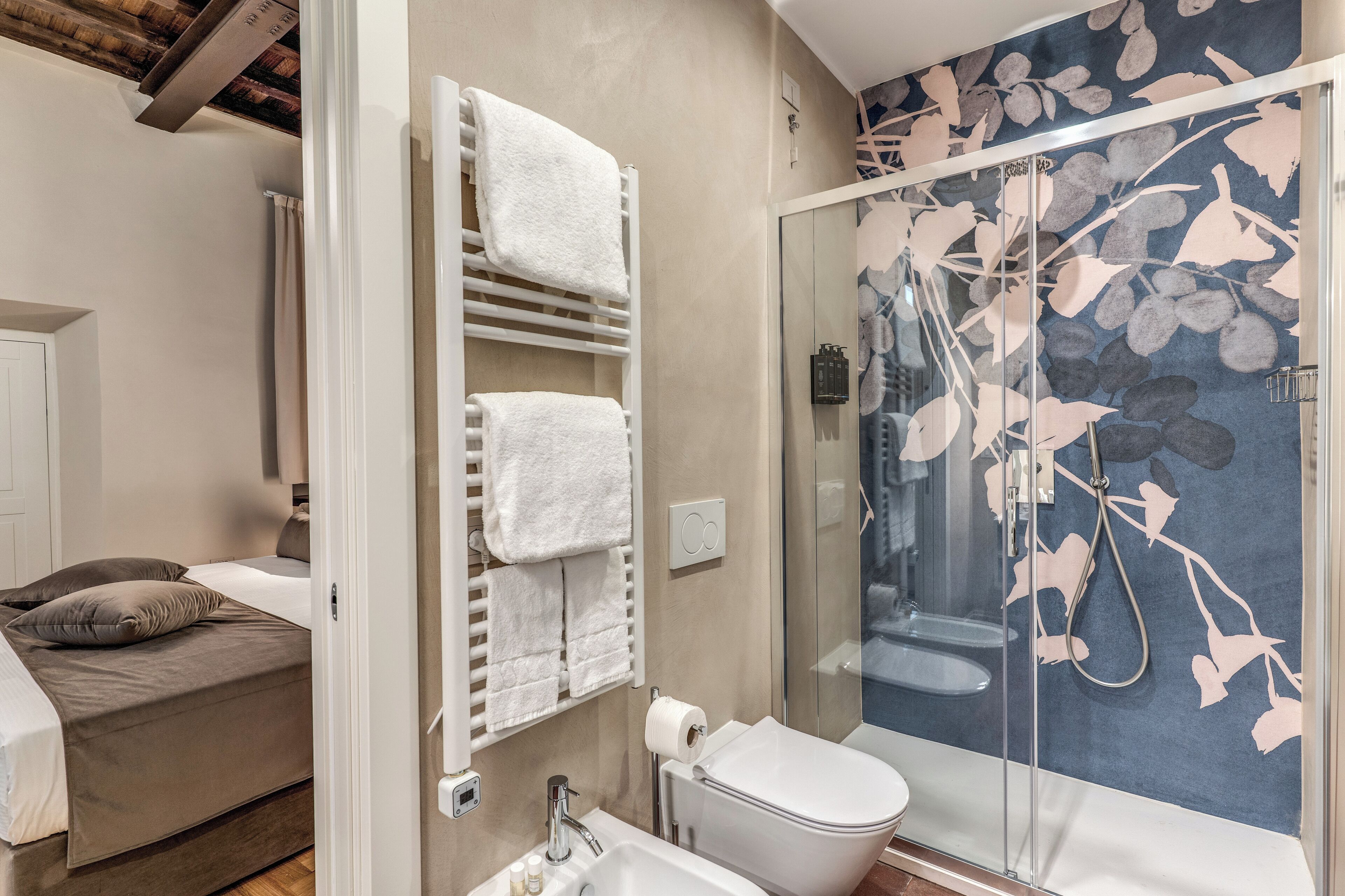Un baño con cabina de ducha de vidrio, inodoro y toallero con varias toallas.