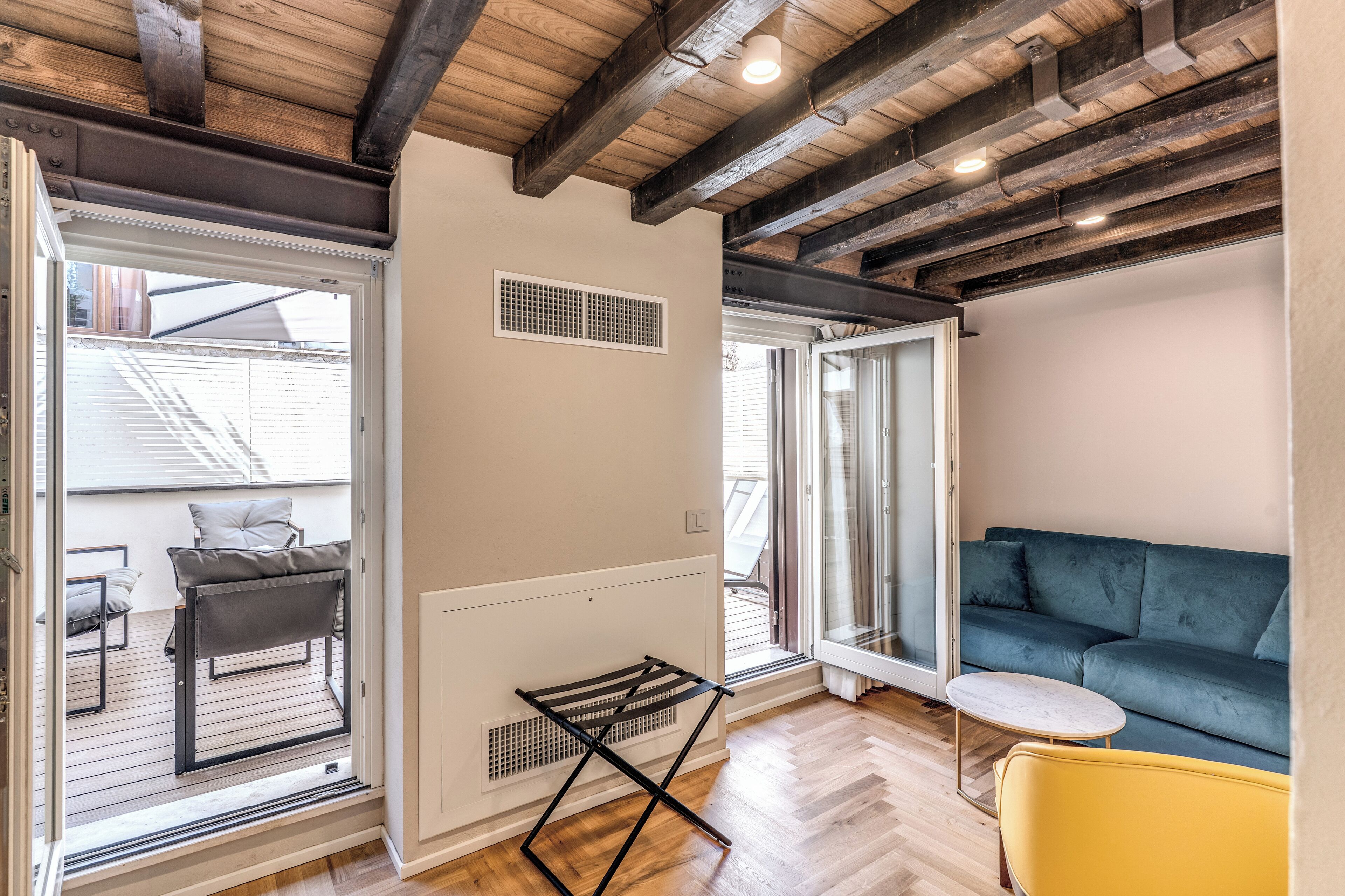 A room with a wooden ceiling, a grey sofa, a yellow chair, and a small table.