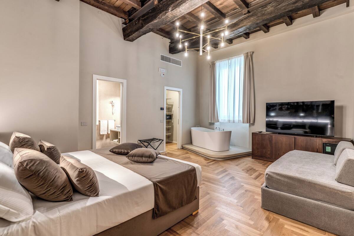 A modern bedroom with a large bed, a sofa, a TV, and a bathroom.