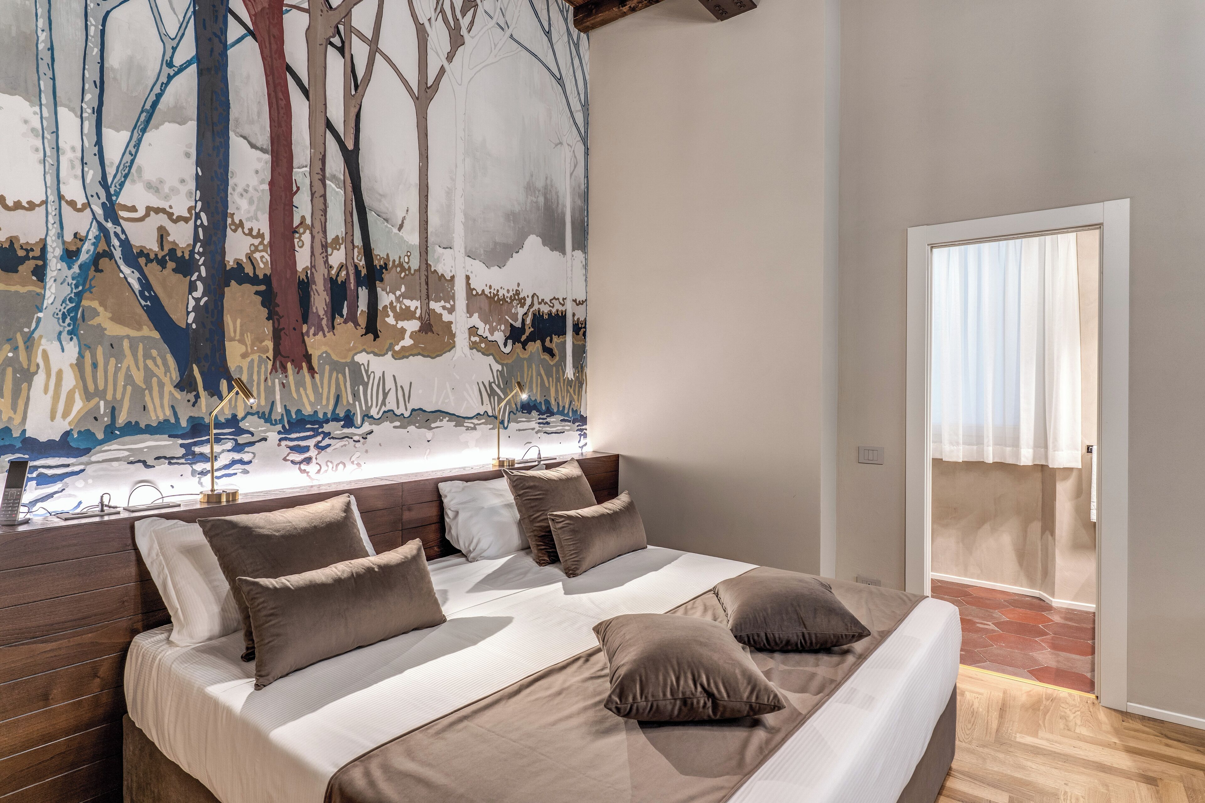 A modern bedroom with a large bed, multiple pillows, a wooden headboard, and a large abstract painting on the wall.