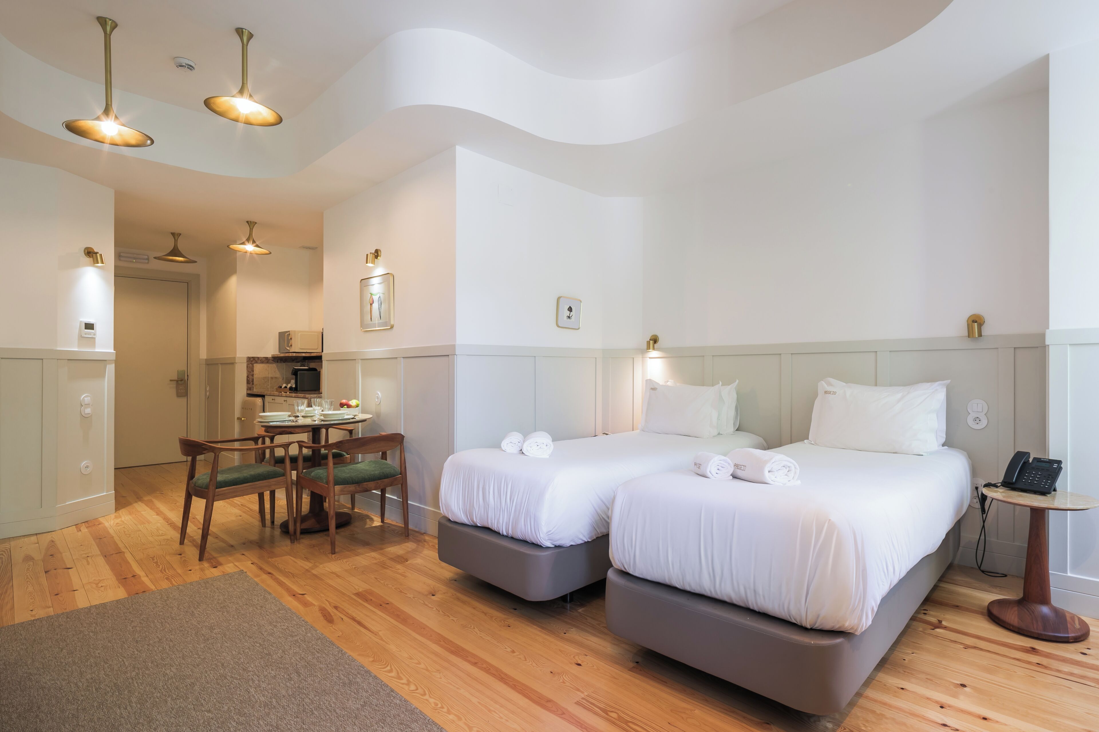 Habitación de hotel con dos camas, zona de comedor y kitchenette.