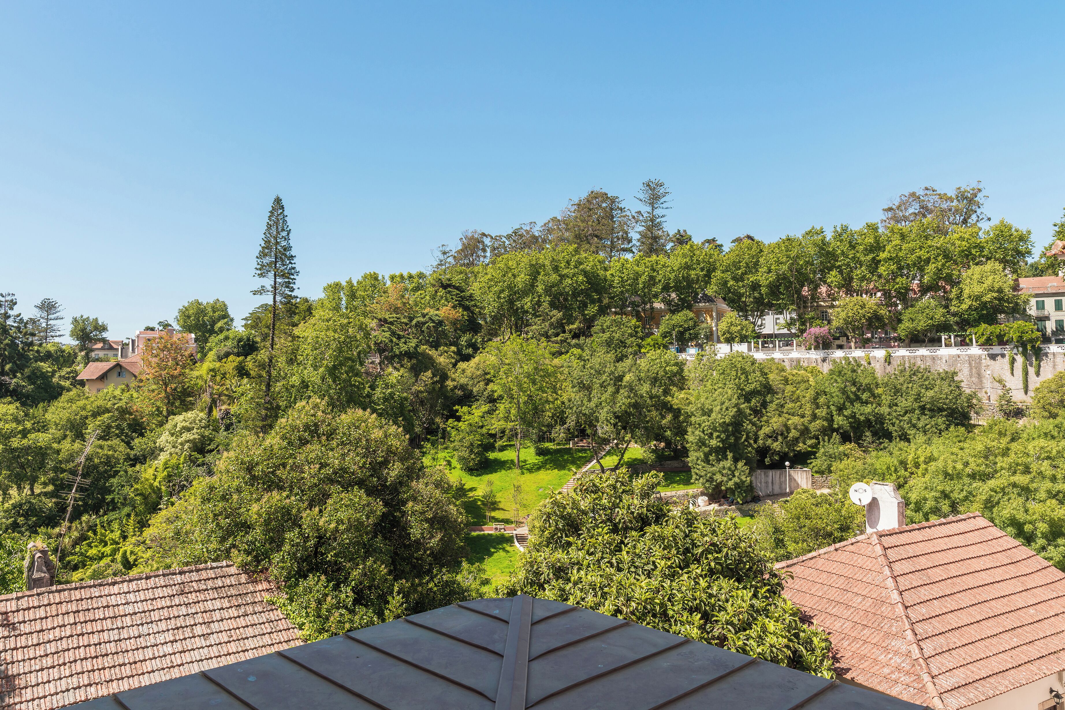 A residential area with a hilltop view, including a house with a tiled roof and a garden.