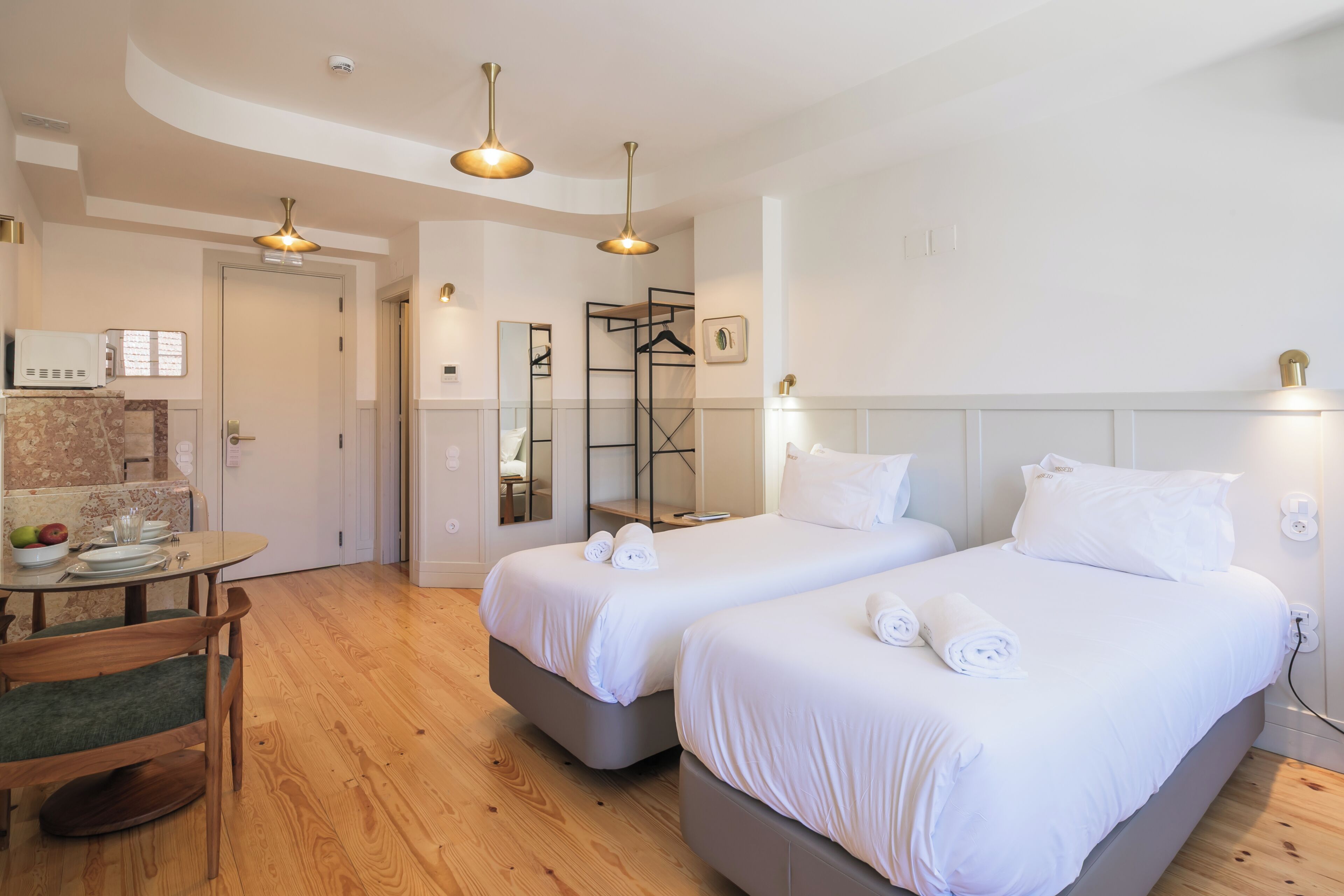 A hotel room with two beds, a dining table, and a kitchen area.