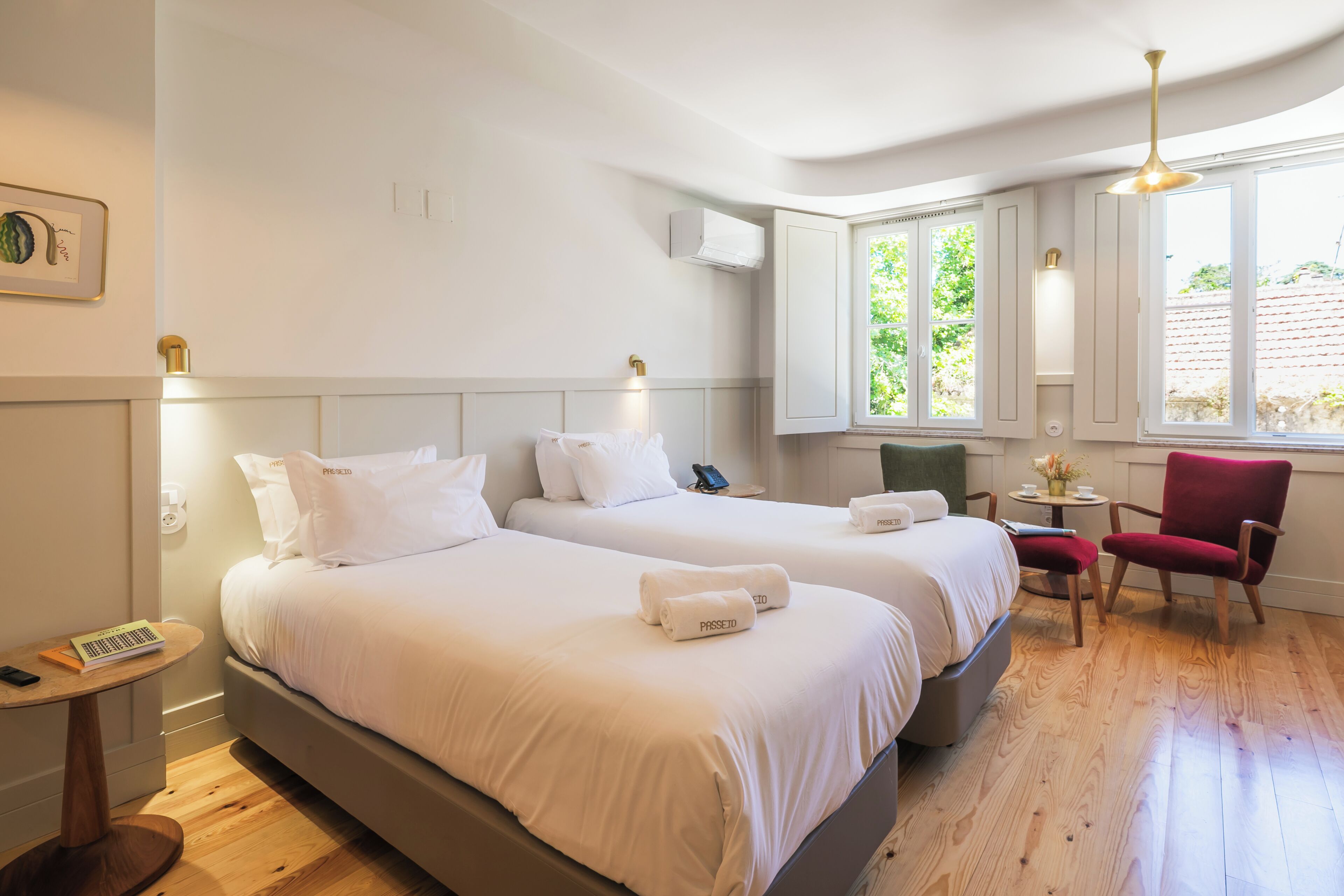 Une chambre d’hôtel avec deux lits, une petite table, une chaise et une fenêtre donnant sur un paysage verdoyant.